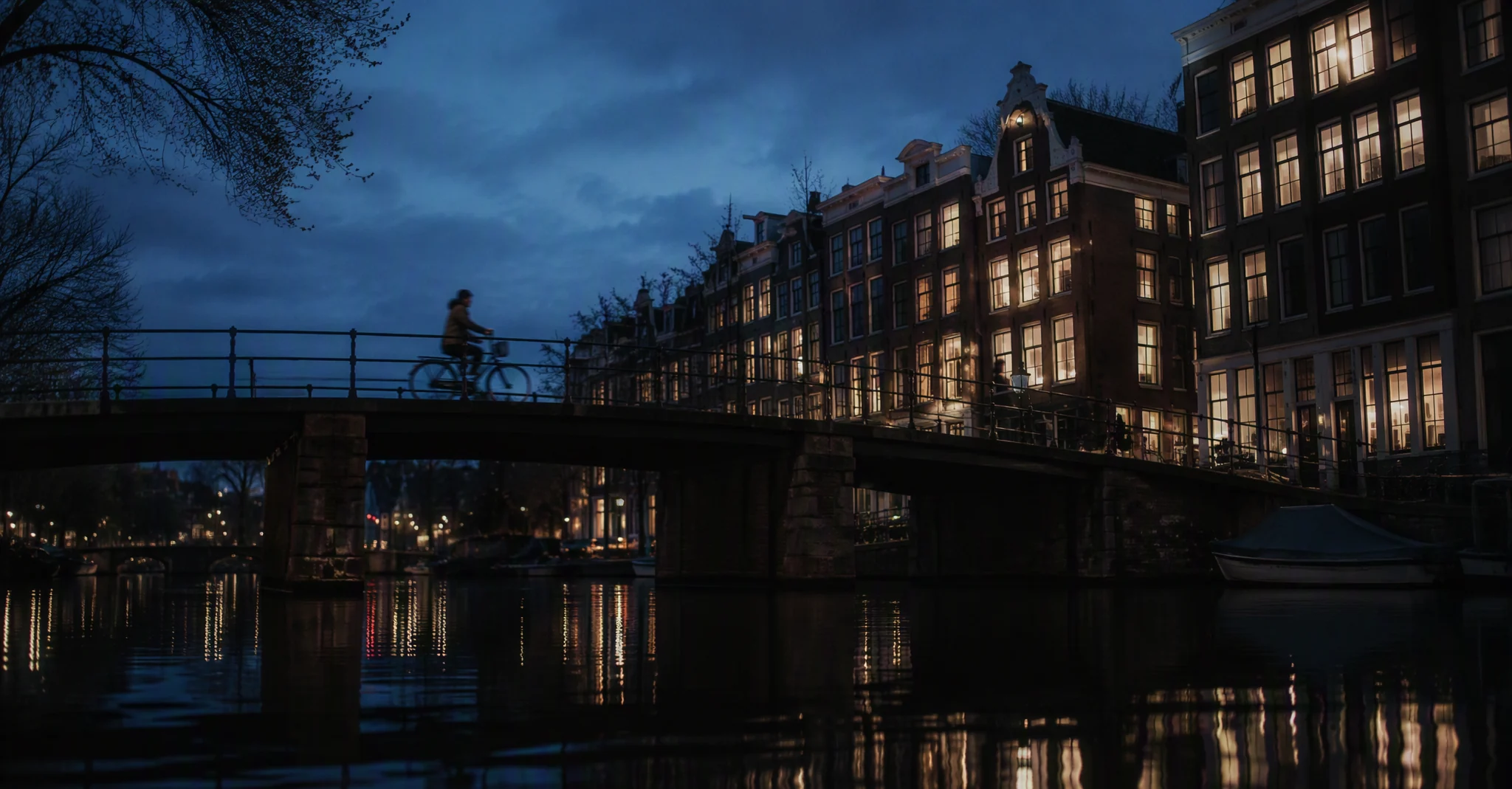 an amsterdam canal at blue hour, warm windows reflected in still water