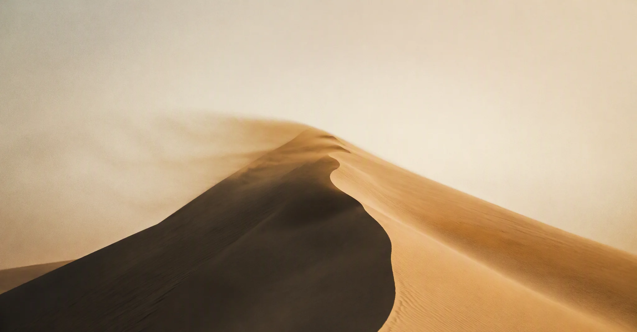 a desert dune ridge at golden hour, sand vapor streaming off the crest